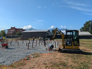 Office Building - Compact excavator driving piles across the pad while the crew checks each position